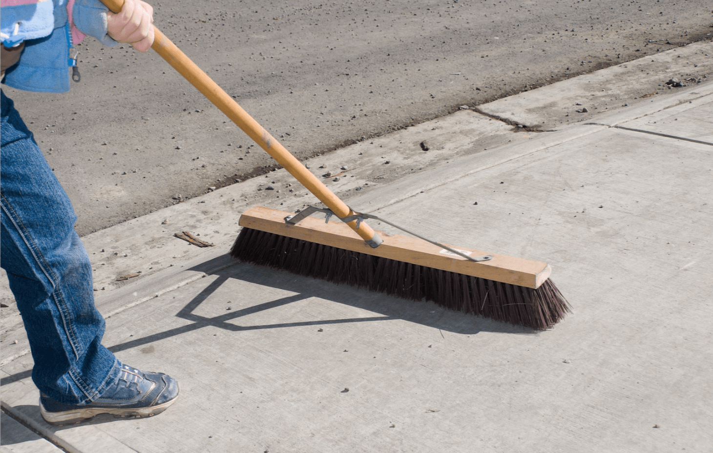 Sweeping Cleaning Concrete Sidewalk With Wide Broom