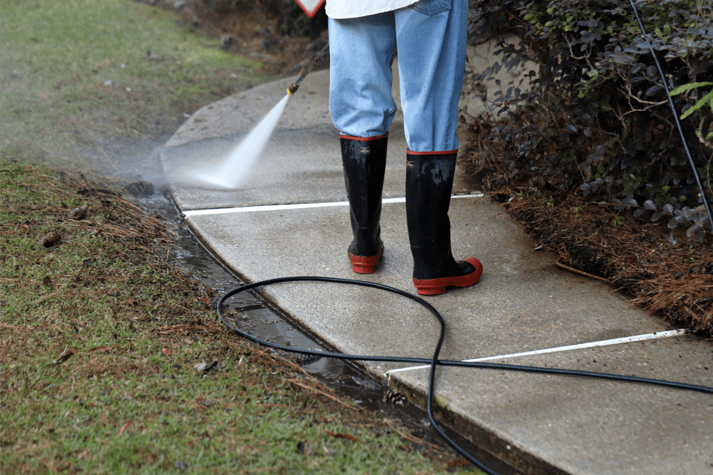 Worker pressure washing conrete sidewalk to clean it